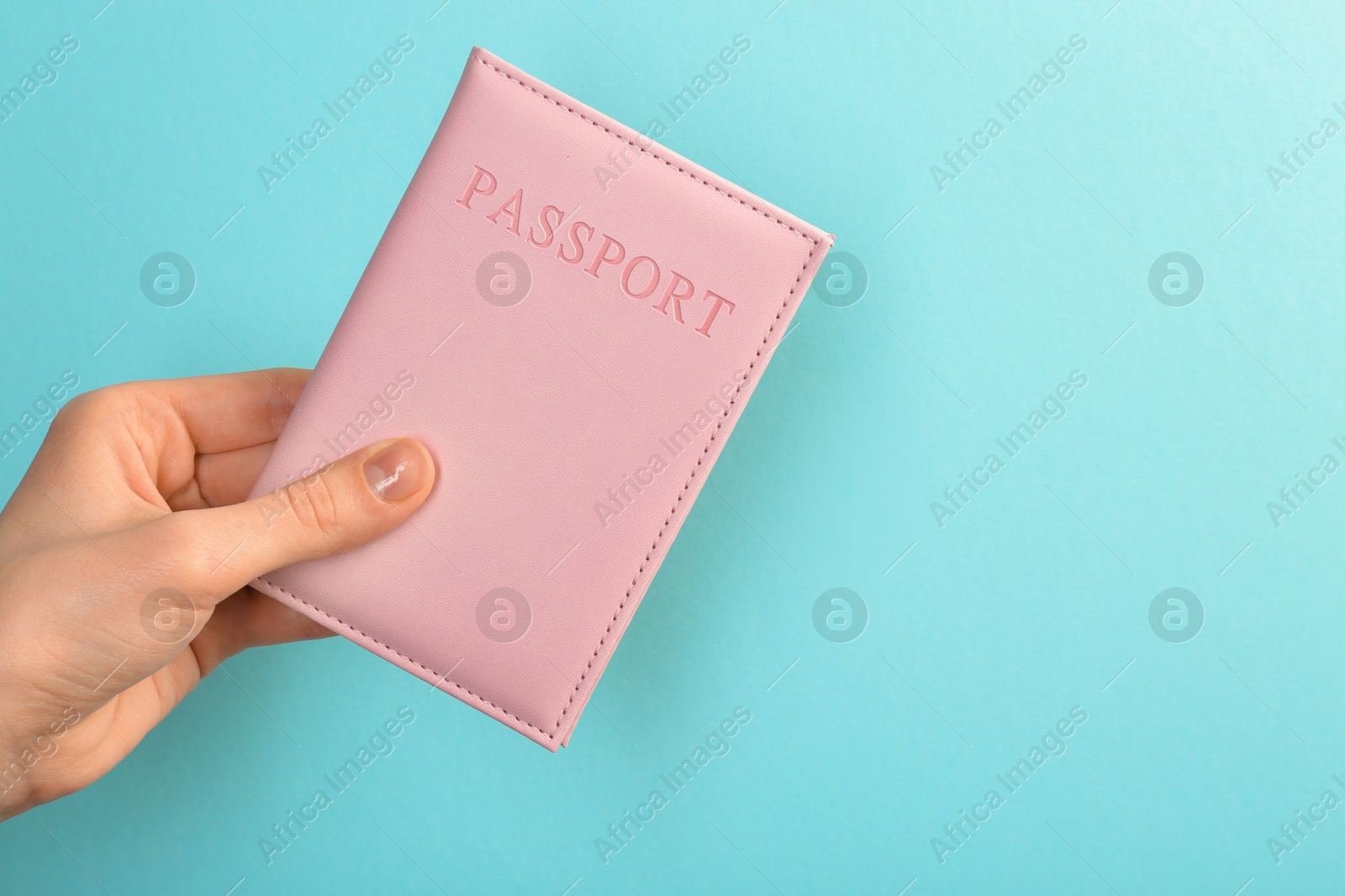 Photo of Woman holding passport in pink cover on turquoise background, closeup. Space for text