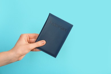 Photo of Woman holding passport in dark blue cover on turquoise background, closeup