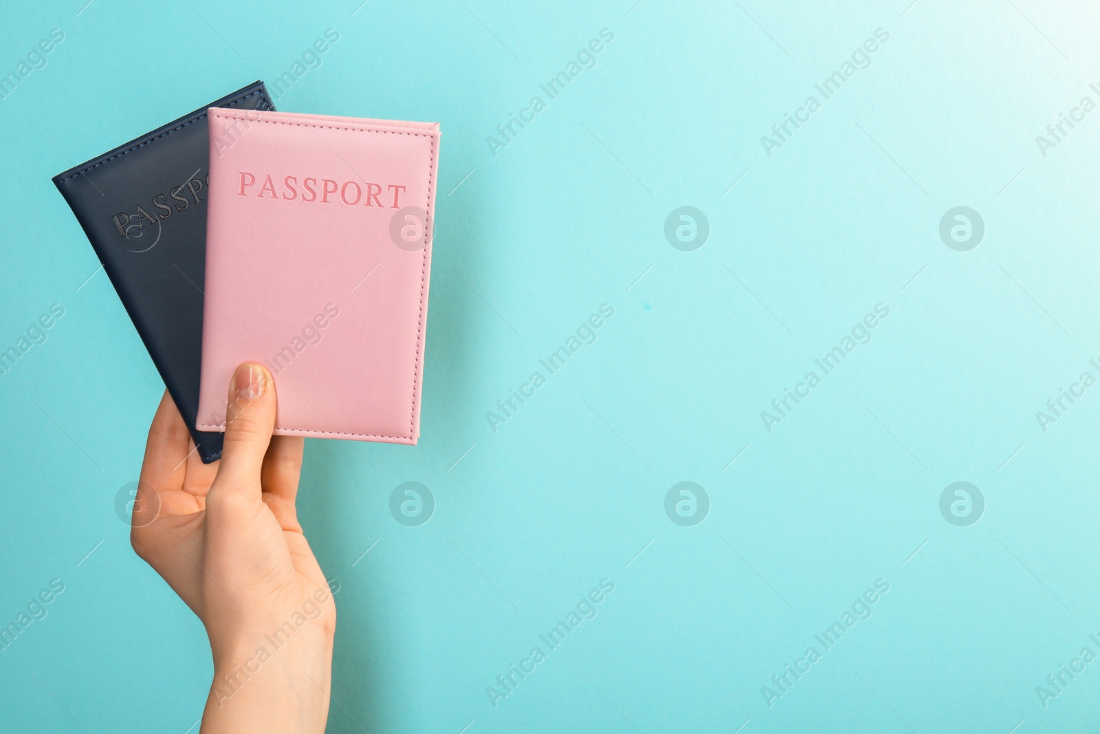 Photo of Woman holding passports in color covers on turquoise background, closeup. Space for text