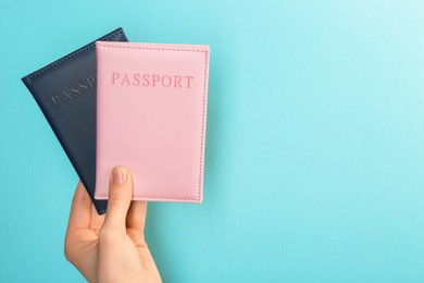 Photo of Woman holding passports in color covers on turquoise background, closeup. Space for text