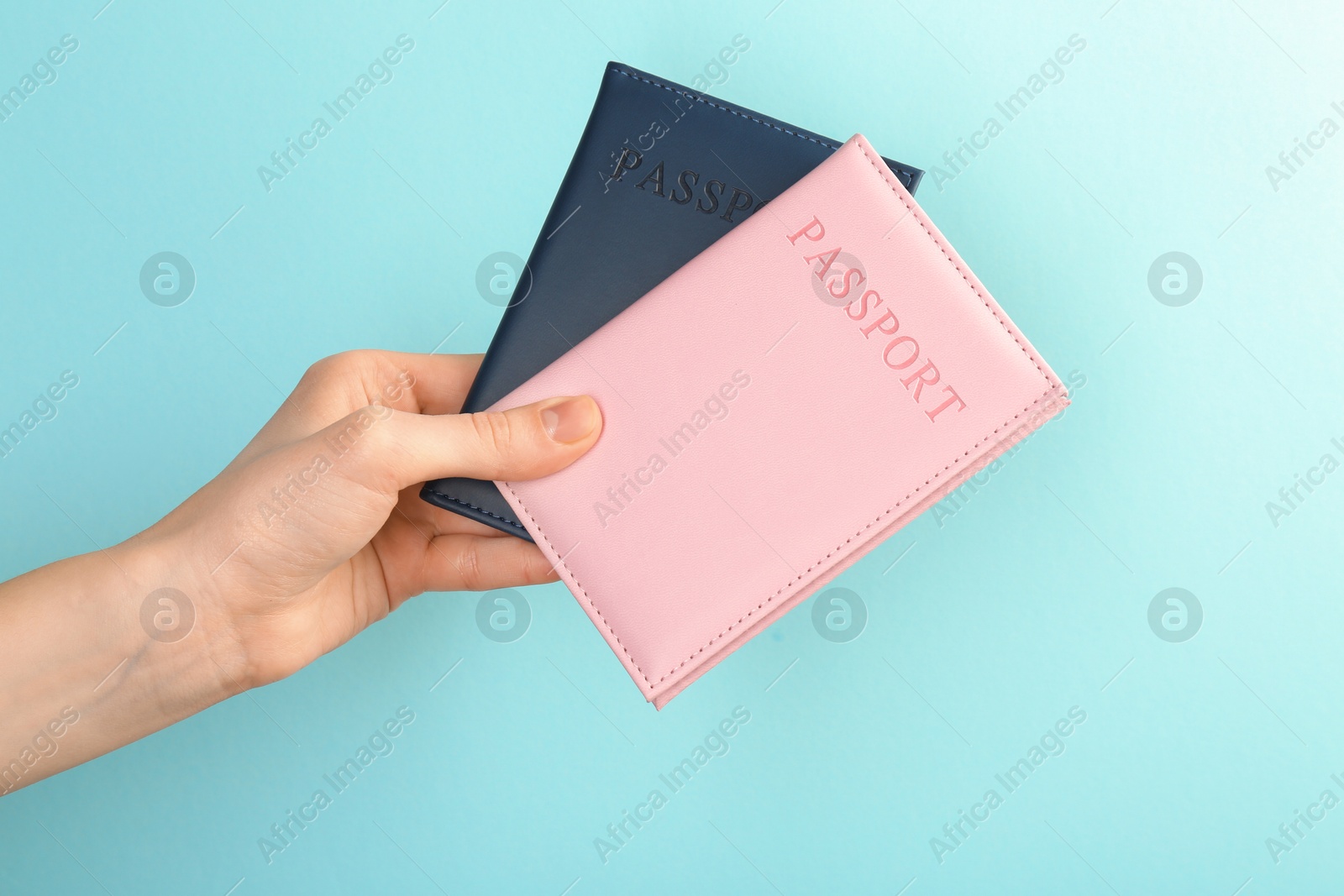 Photo of Woman holding passports in color covers on turquoise background, closeup