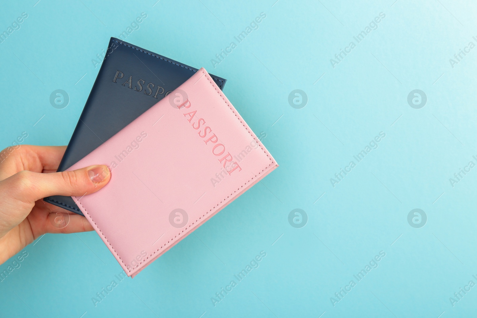 Photo of Woman holding passports in color covers on turquoise background, closeup. Space for text