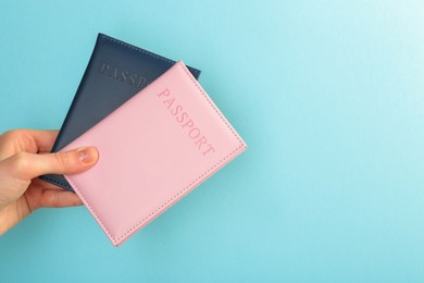 Photo of Woman holding passports in color covers on turquoise background, closeup. Space for text