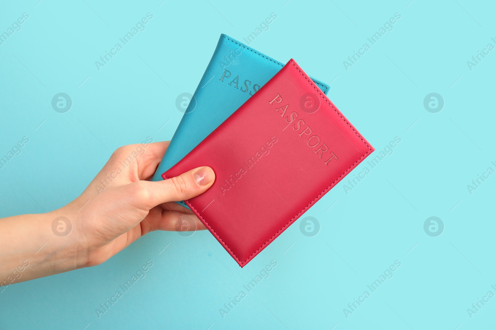 Photo of Woman holding passports in color covers on turquoise background, closeup