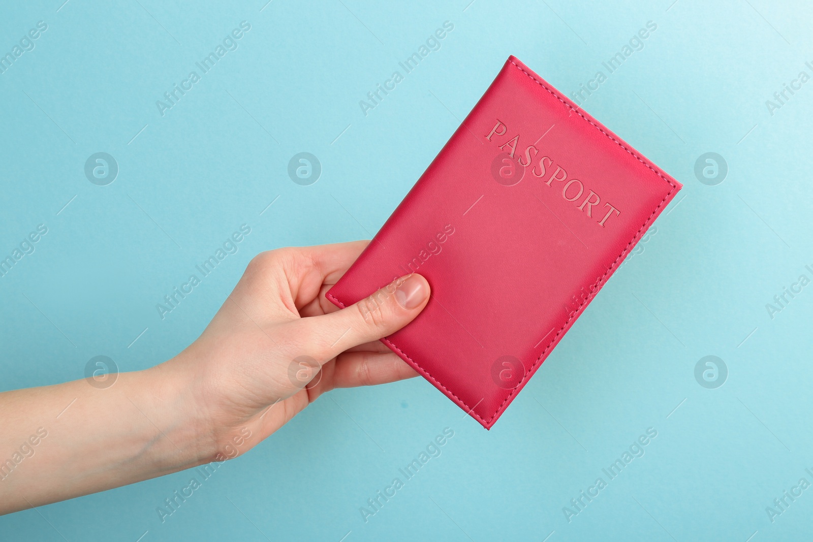 Photo of Woman holding passport in pink cover on turquoise background, closeup