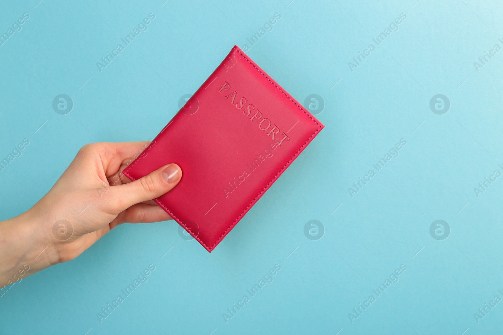 Photo of Woman holding passport in pink cover on turquoise background, closeup. Space for text