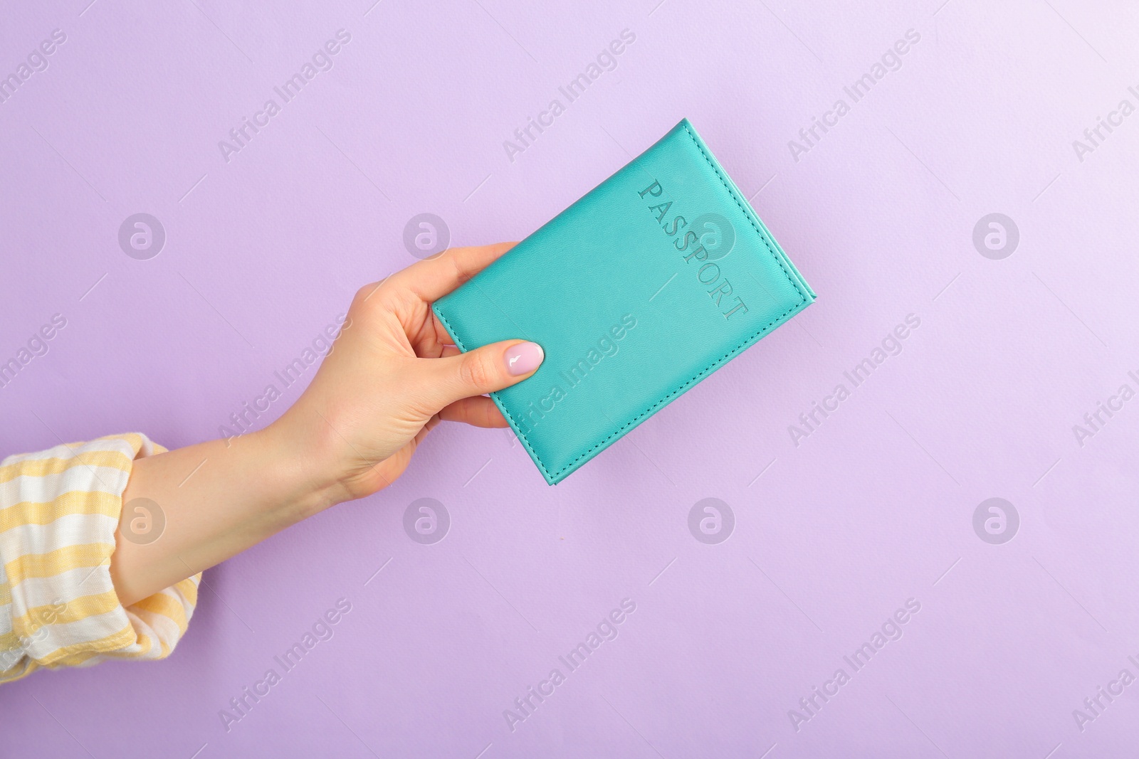 Photo of Woman holding passport in turquoise cover on violet background, closeup