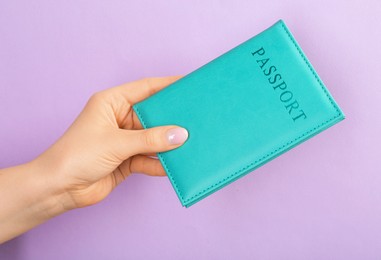 Photo of Woman holding passport in turquoise cover on violet background, closeup