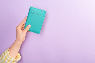 Photo of Woman holding passport in turquoise cover on violet background, closeup. Space for text