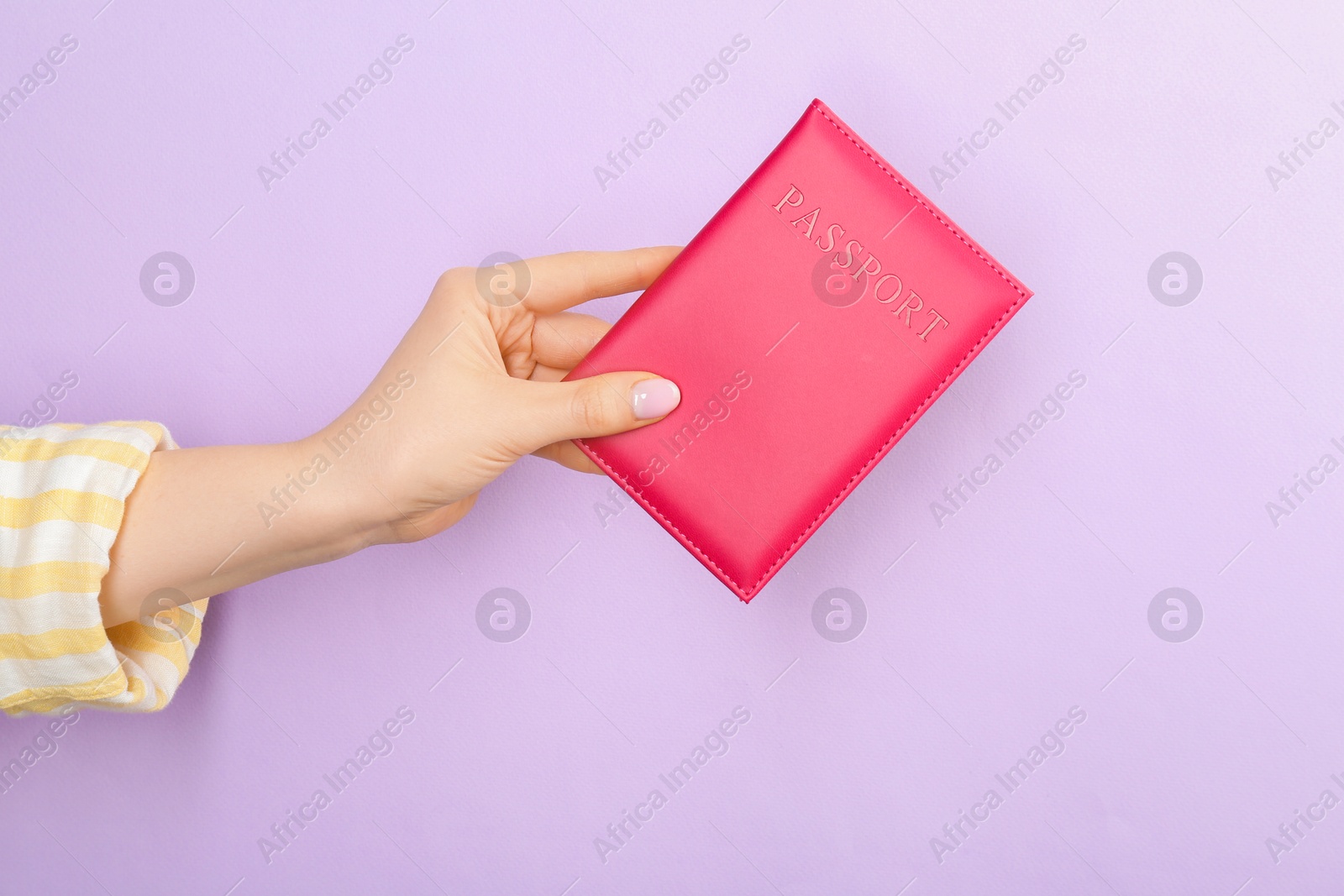 Photo of Woman holding passport in pink cover on violet background, closeup