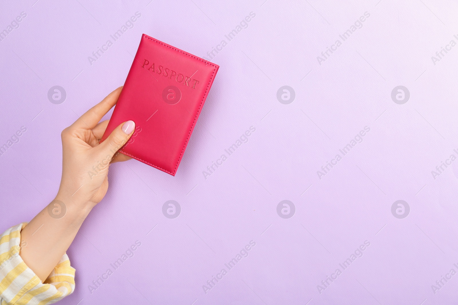 Photo of Woman holding passport in pink cover on violet background, closeup. Space for text