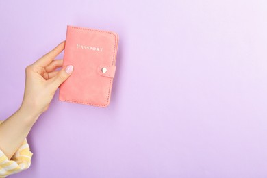 Photo of Woman holding passport in pink cover on violet background, closeup. Space for text