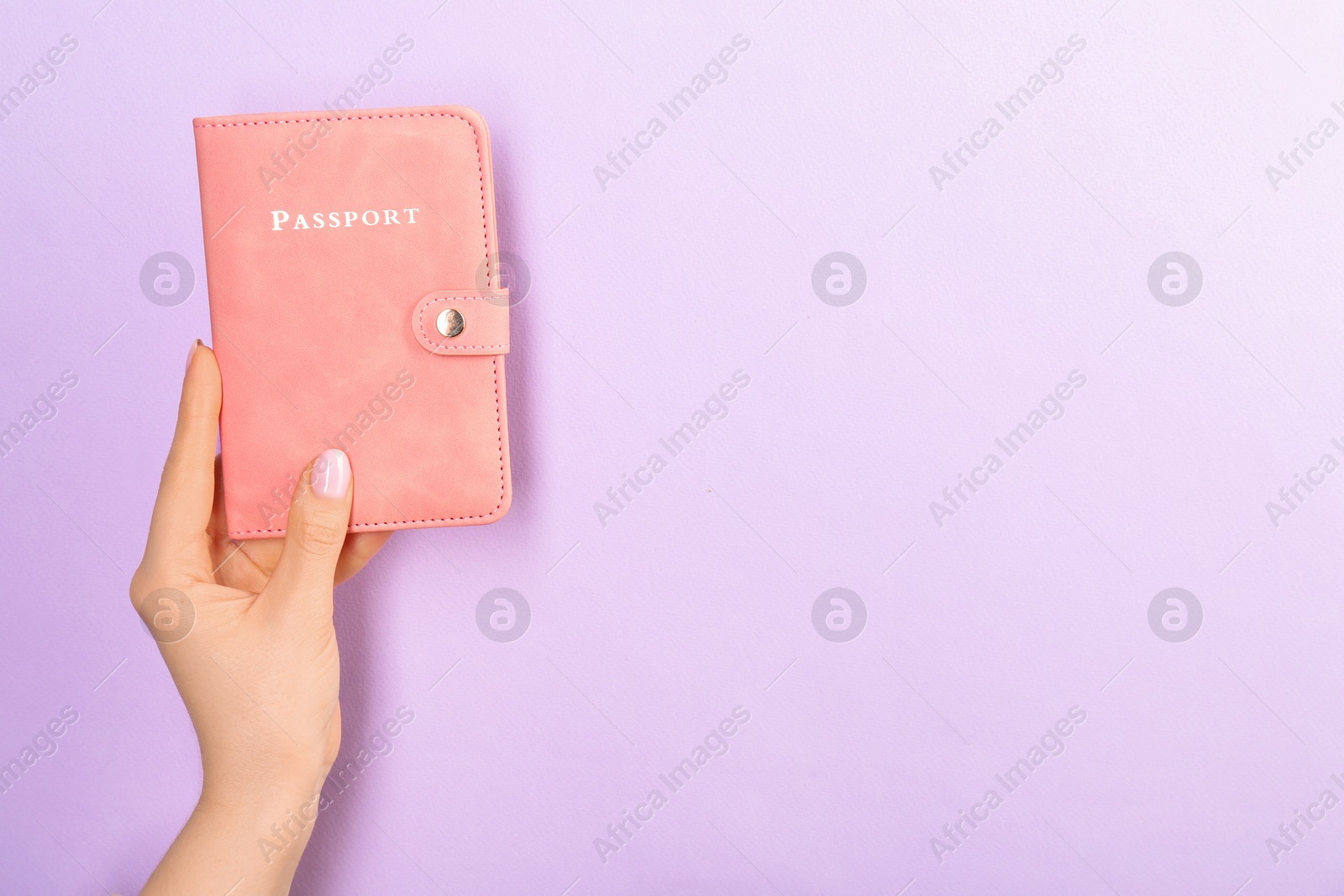 Photo of Woman holding passport in pink cover on violet background, closeup. Space for text