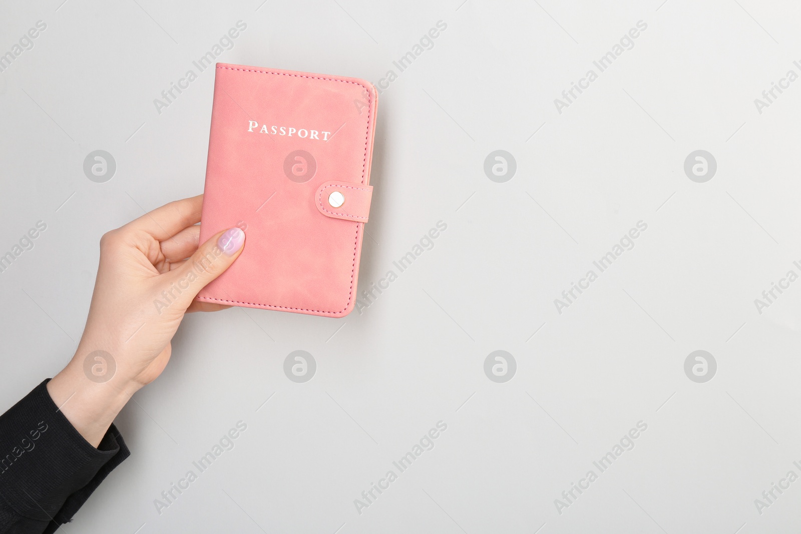 Photo of Woman holding passport in pink cover on light grey background, closeup. Space for text