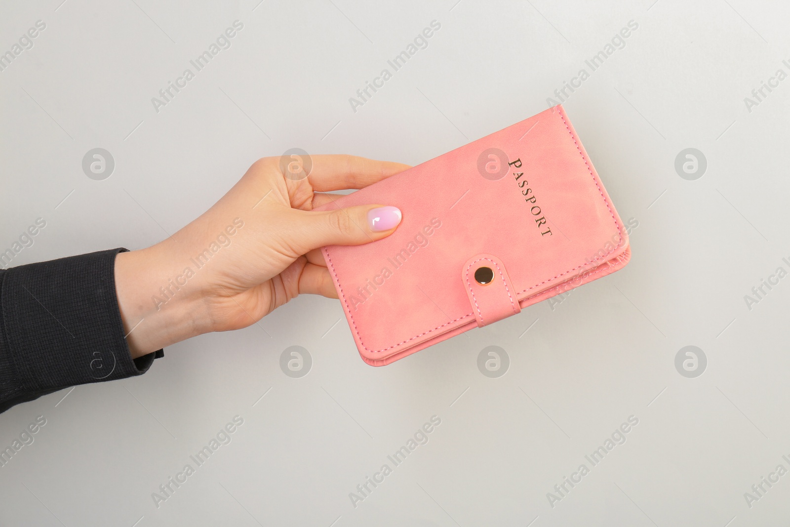 Photo of Woman holding passport in pink cover on light grey background, closeup