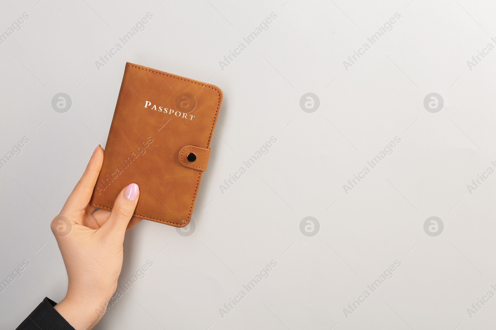 Photo of Woman holding passport in brown cover on light grey background, closeup. Space for text