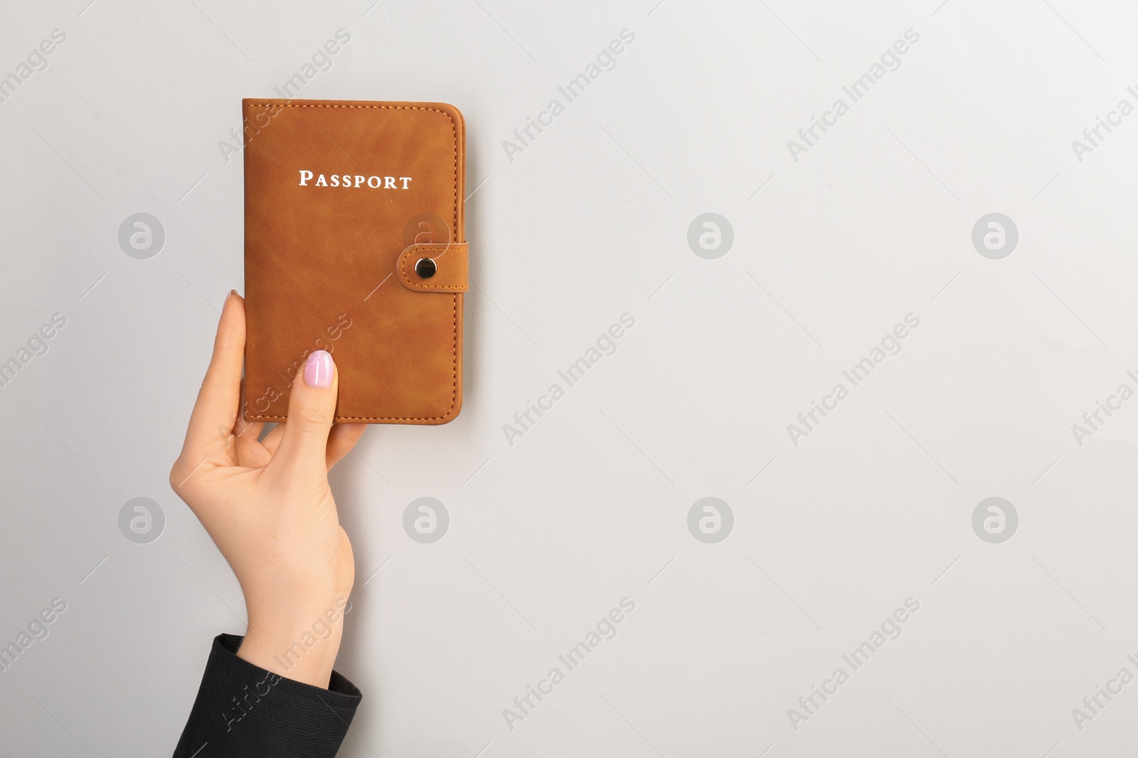 Photo of Woman holding passport in brown cover on light grey background, closeup. Space for text