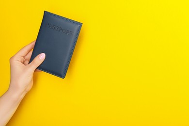 Photo of Woman holding passport in dark blue cover on yellow background, closeup. Space for text