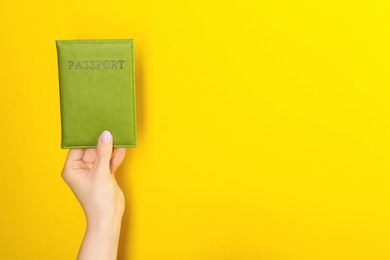 Photo of Woman holding passport in green cover on yellow background, closeup. Space for text