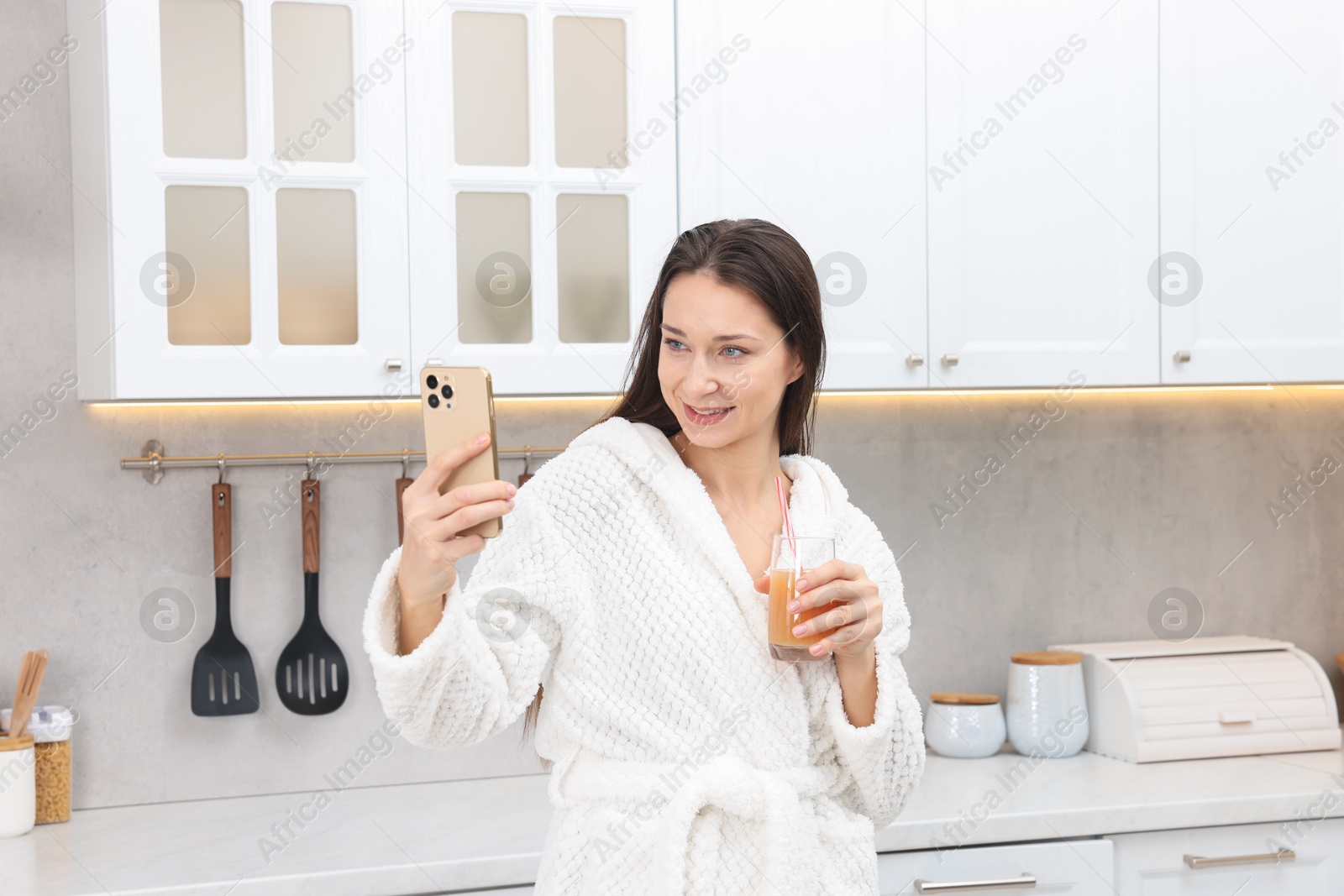 Photo of Beautiful woman with glass of juice taking selfie after spa procedure in kitchen