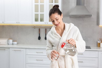 Photo of Beautiful woman pouring water into glass after spa procedure in kitchen, space for text