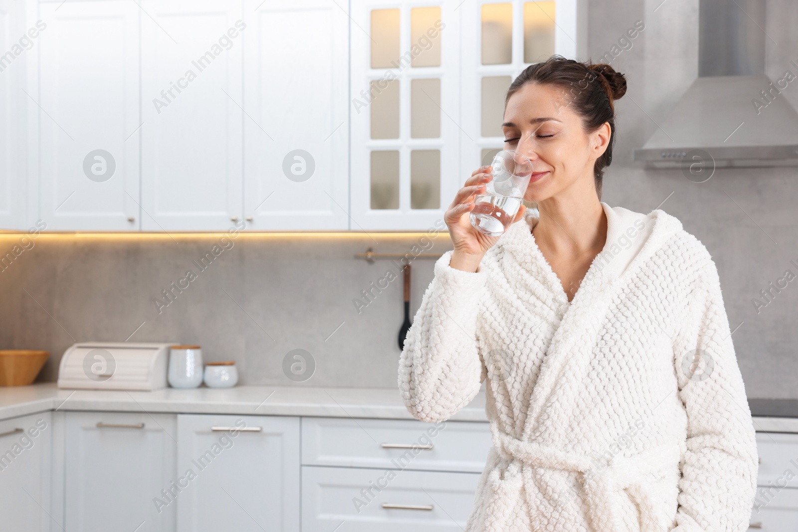 Photo of Beautiful woman drinking water after spa procedure in kitchen, space for text