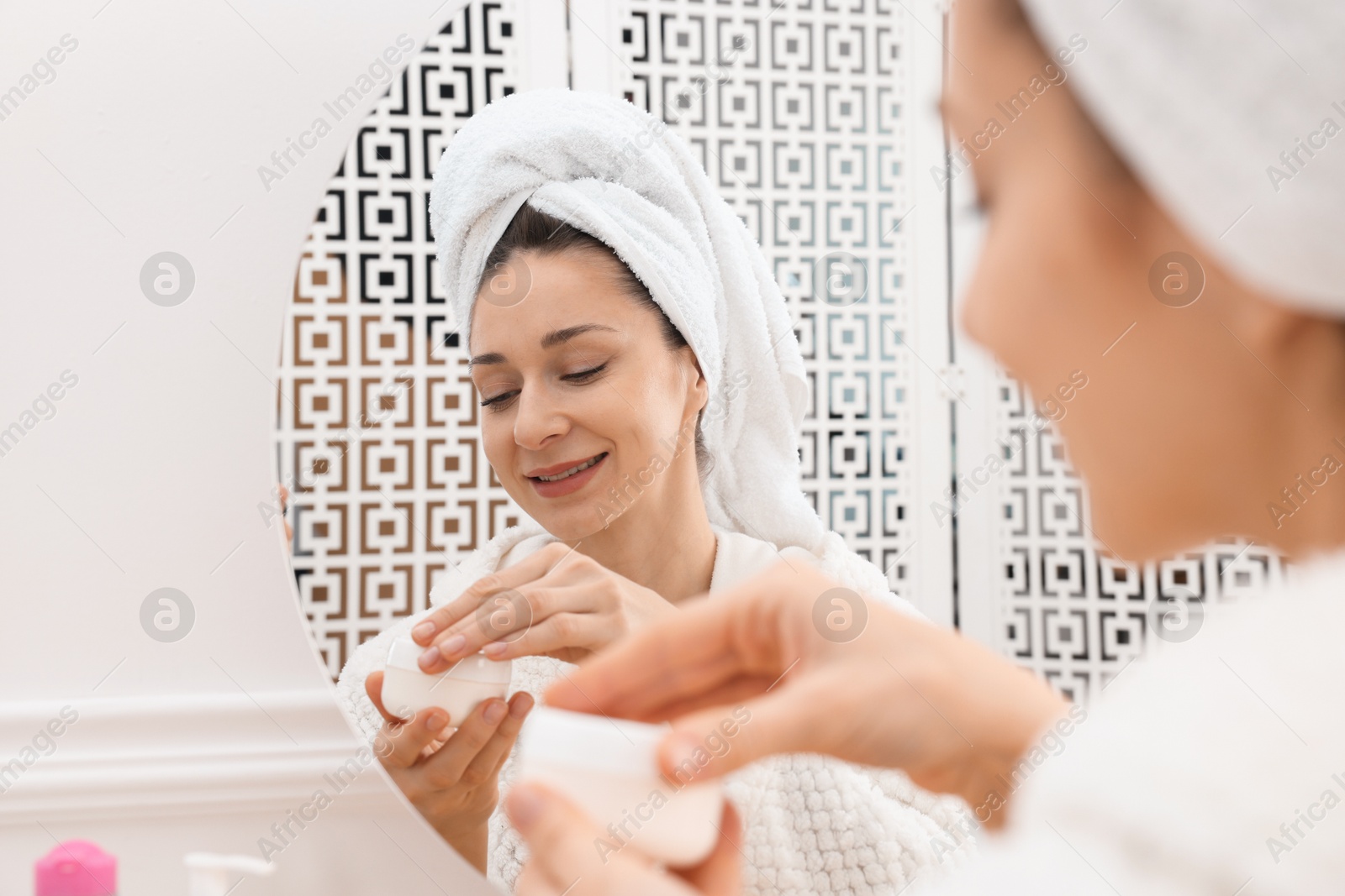 Photo of Spa day. Beautiful woman with cream near mirror indoors