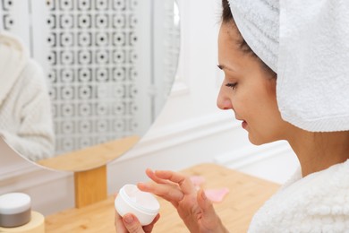 Photo of Spa day. Beautiful woman with cream near mirror indoors