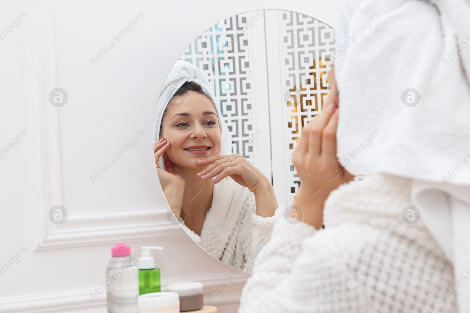 Photo of Spa day. Beautiful woman with towel on head near mirror indoors