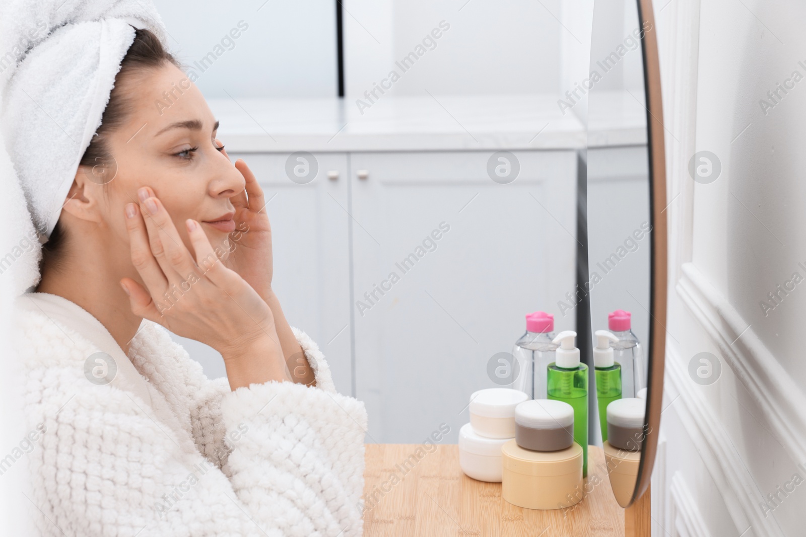 Photo of Spa day. Beautiful woman with towel on head near mirror indoors