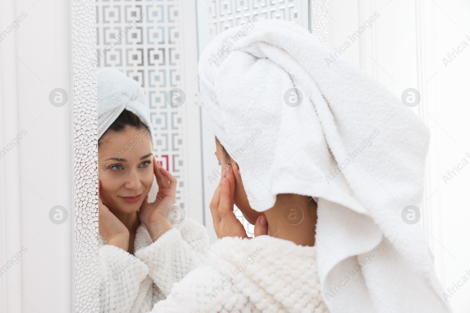 Photo of Spa day. Beautiful woman with towel on head near mirror indoors