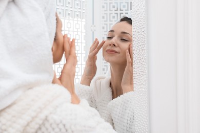 Photo of Spa day. Beautiful woman with towel on head near mirror indoors