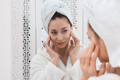 Photo of Spa day. Beautiful woman with towel on head near mirror indoors