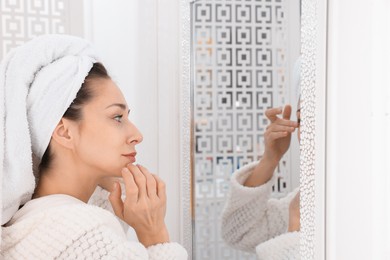 Photo of Spa day. Beautiful woman with towel on head near mirror indoors