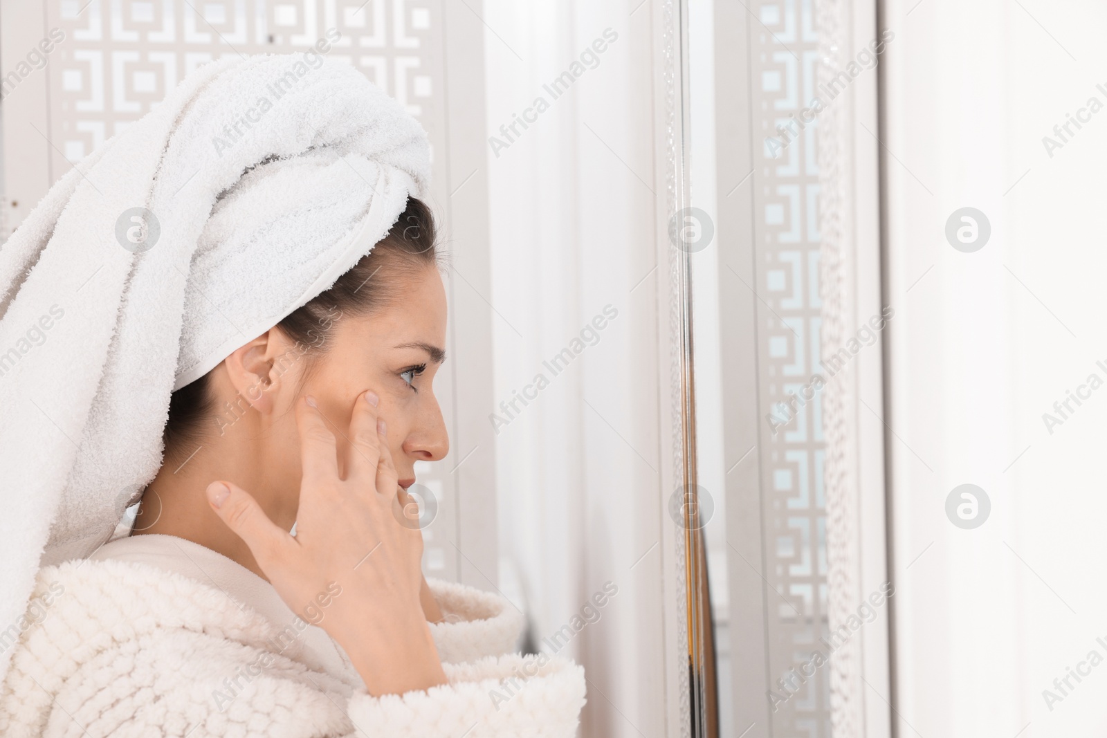 Photo of Spa day. Beautiful woman with towel on head near mirror indoors