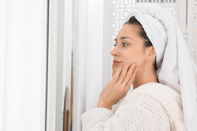 Photo of Spa day. Beautiful woman with towel on head near mirror indoors