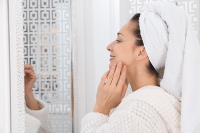 Photo of Spa day. Beautiful woman with towel on head near mirror indoors