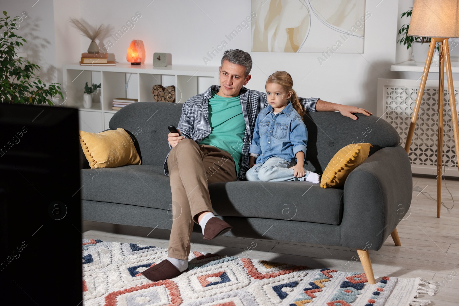 Photo of Father and his daughter watching TV on sofa at home