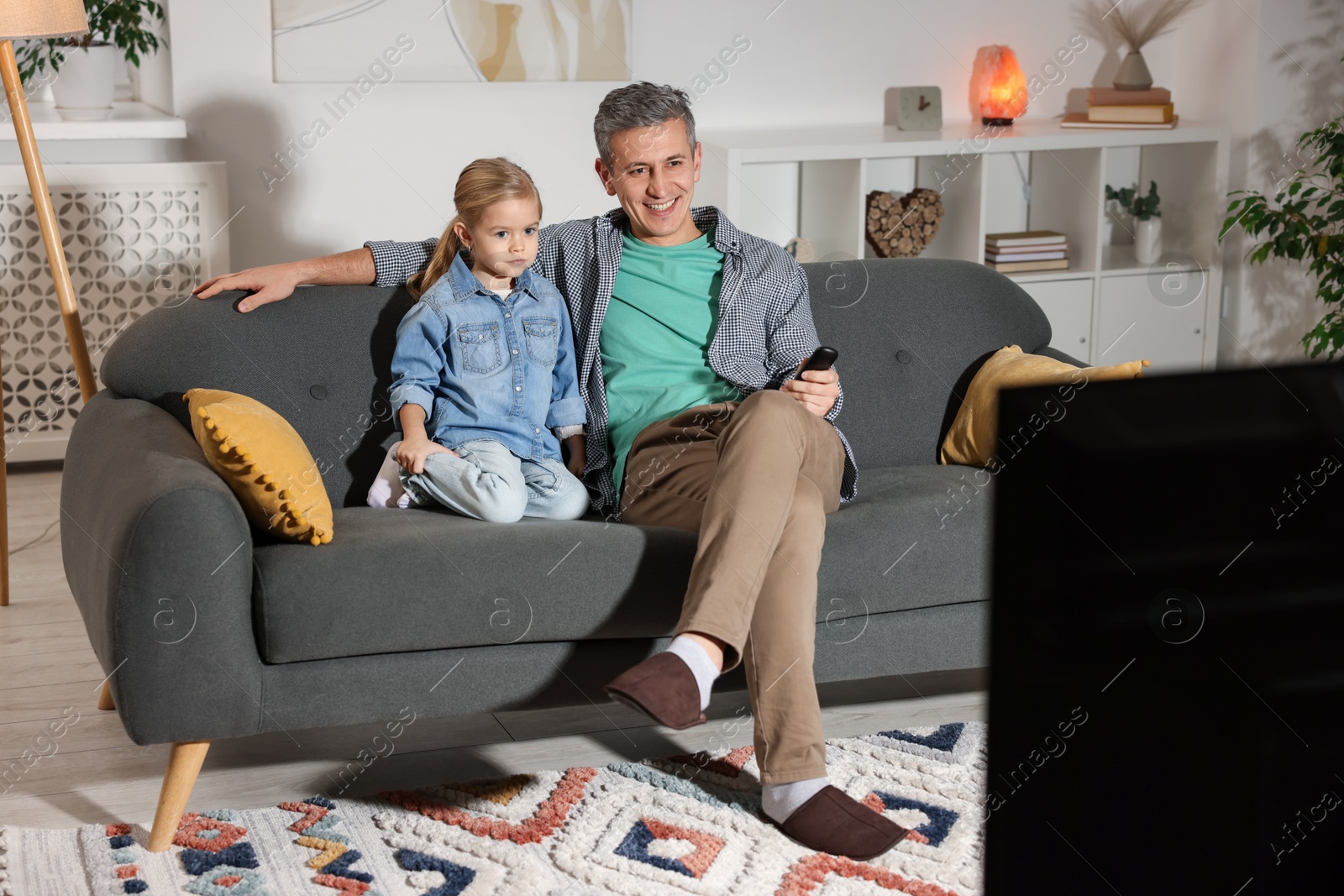 Photo of Father and his daughter watching TV on sofa at home