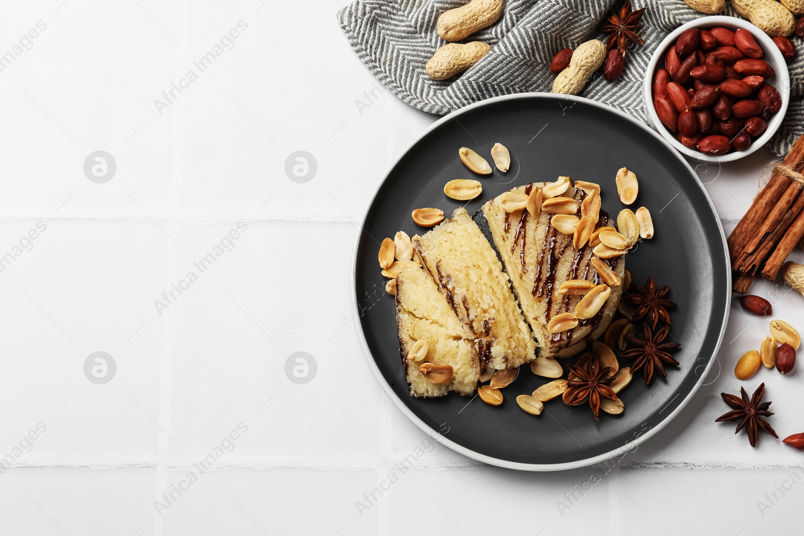 Photo of Delicious sweet semolina halva with peanuts and spices on white tiled table, flat lay. Space for text