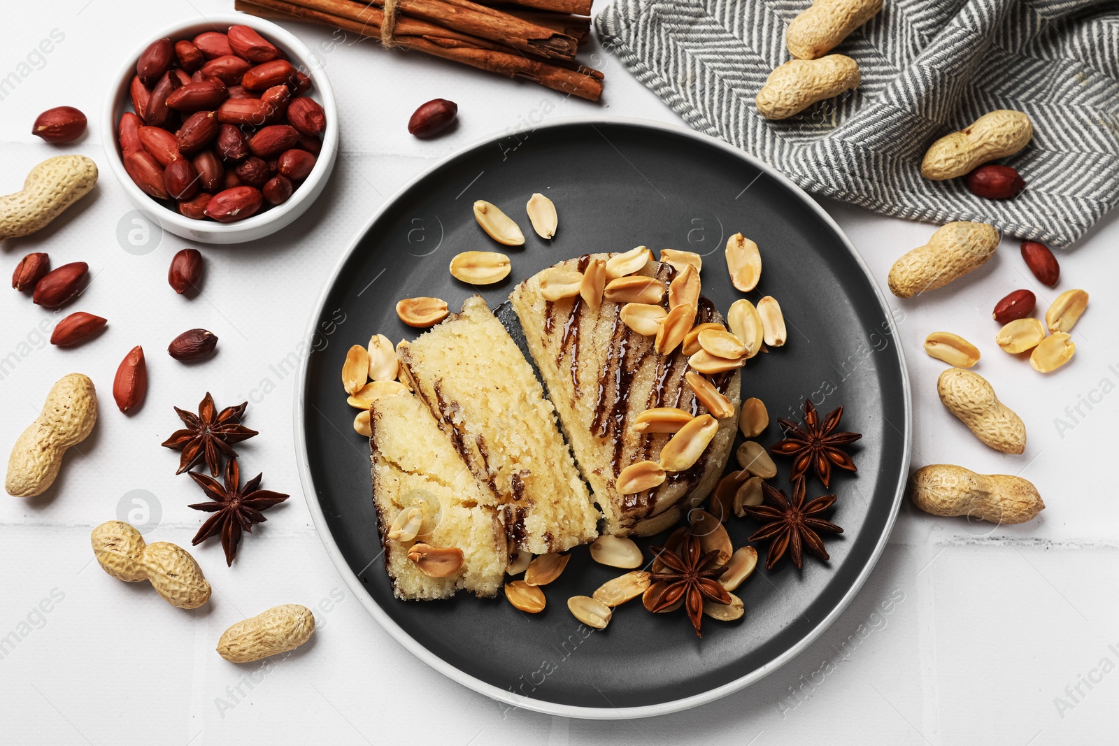 Photo of Delicious sweet semolina halva with peanuts and spices on white tiled table, flat lay