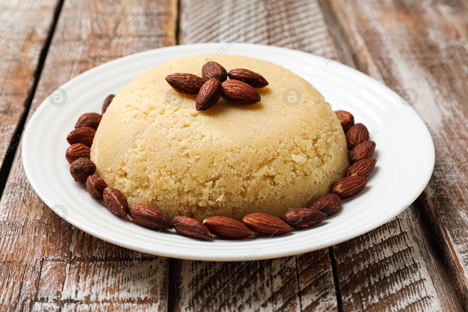 Photo of Delicious sweet semolina halva with almond on wooden table, closeup