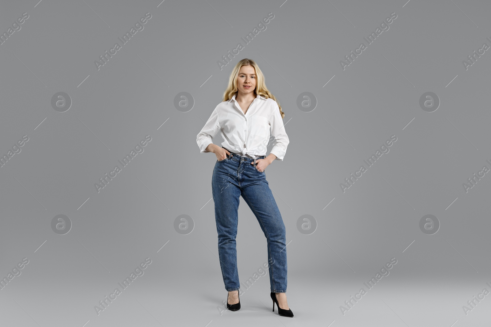 Photo of Smiling woman in stylish jeans on grey background