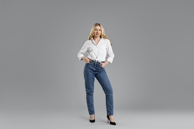 Photo of Smiling woman in stylish jeans on grey background