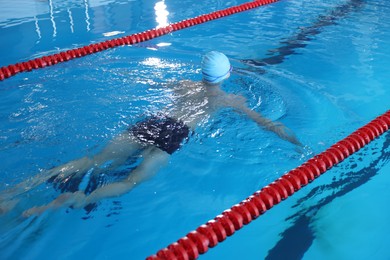 Photo of Young man in cap and swimwear swimming in pool indoors