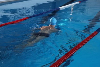 Photo of Young man in cap and swimwear swimming in pool indoors