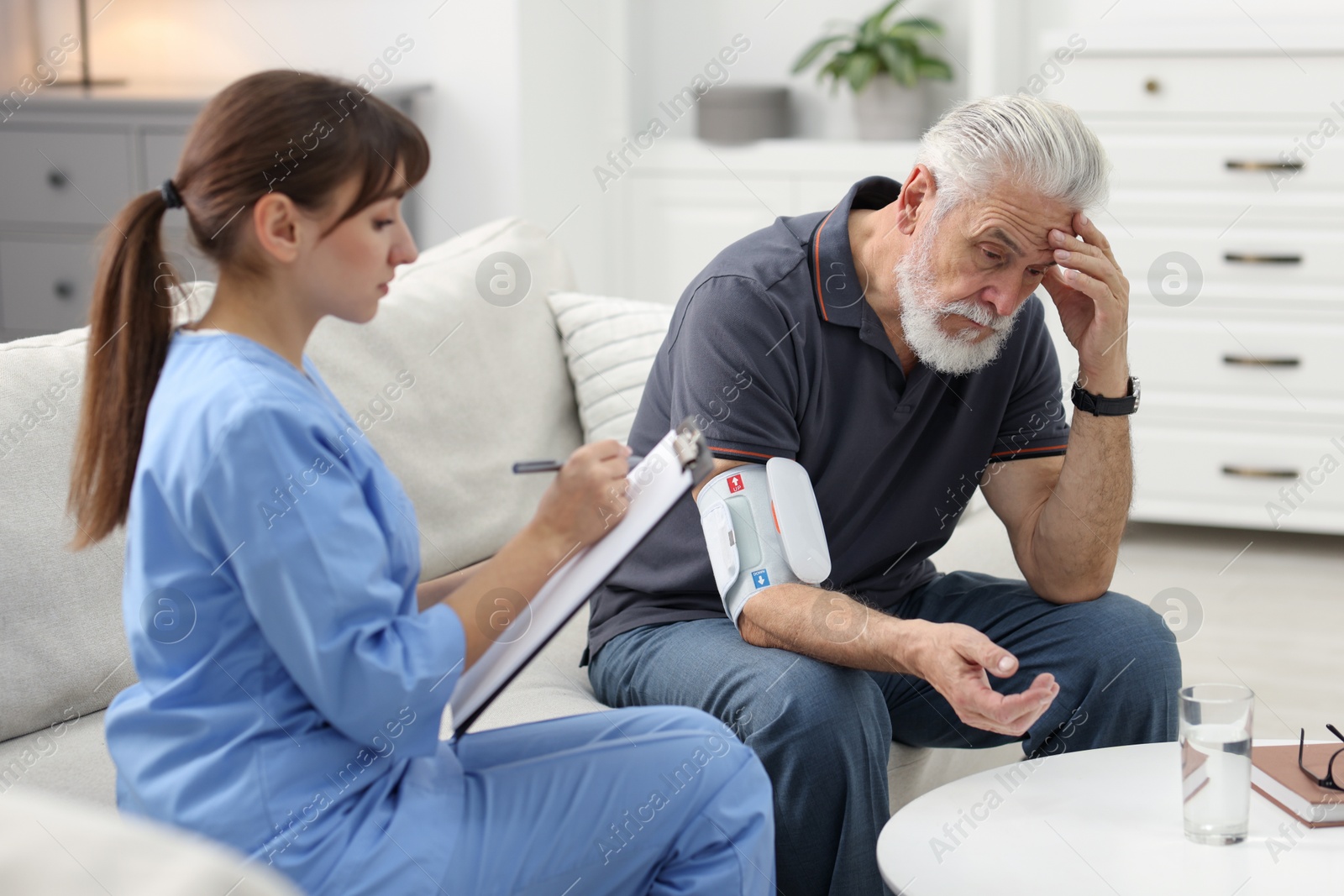 Photo of Nurse measuring senior man's blood pressure and writing results at home