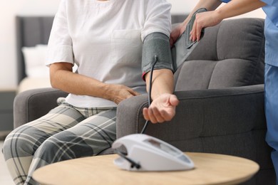 Photo of Nurse measuring senior woman's blood pressure at home, closeup