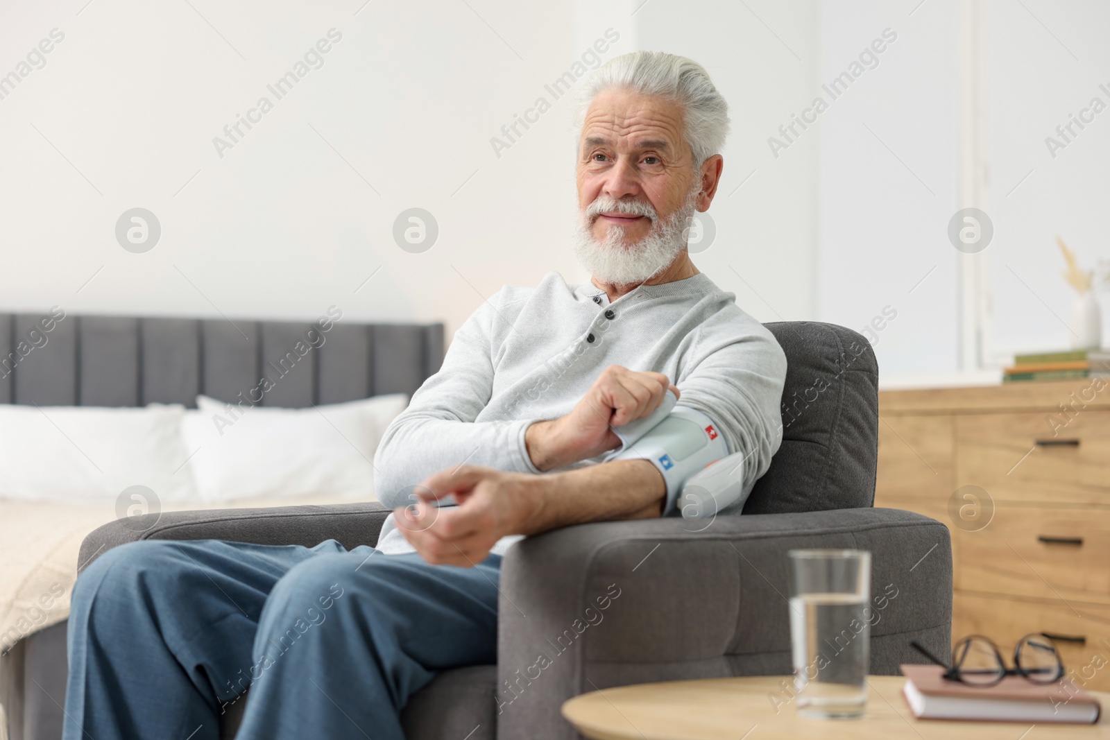 Photo of Senior man measuring blood pressure in armchair at home