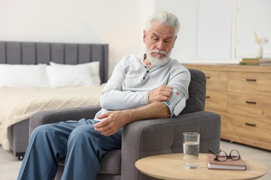 Photo of Senior man measuring blood pressure in armchair at home